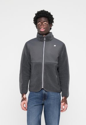 Gray fleece jacket with a high collar, featuring a front zipper, contrasting sleeves, and a logo on the chest. Smooth and textured materials.