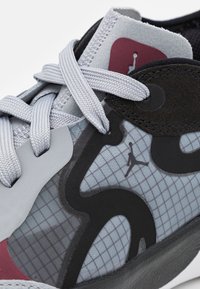 Szare buty sportowe z czarnymi akcentami i siateczkową cholewką. Posiadają szare sznurówki, gładką teksturę oraz czerwoną naszywkę z logo na języku.