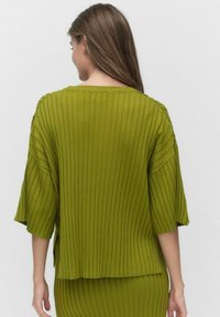 Vihreä uurrettu neulepaita, jossa on 3/4 hihat ja väljät leikkaukset, pyöreä kaula-aukko ja sivuleikkaukset lisäämään mukavuutta.