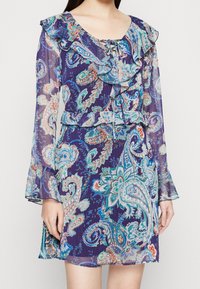 Dlouhé rukávy, fialová šaty s paisley vzorem a volánkovým výstřihem a manžetami. Obsahuje květinové vzory v tyrkysové, růžové a krémové barvě na průhledné látce.
