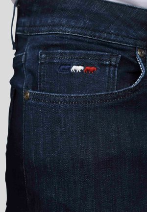 Un jean en denim bleu foncé présente une poche avant avec des motifs d'animaux brodés en rouge, blanc et bleu, un matériel en métal et une coupe classique.