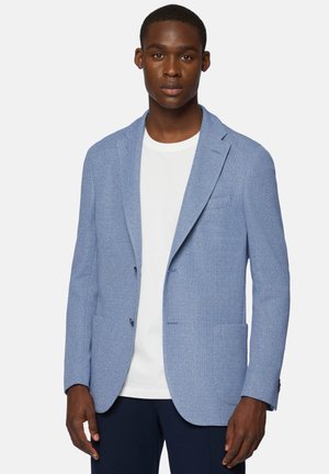 Blazer texturizado azul claro con dos bolsillos frontales y solapas de muesca, llevado sobre una camiseta blanca. Ajuste entallado con detalles de costura visibles.