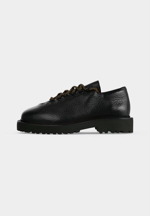 Zwarte gestructureerde leren veterboot met dikke rubberen zool en robuust profiel, zijaanzicht op een effen lichte achtergrond.
