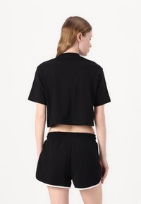 Svart avkortet t-skjorte med korte ermer, laget av bomull. Kombinert med sorte shorts med hvit kant og elastisk midje.