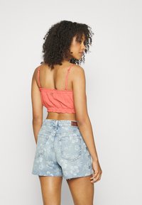 Top cropped em coral com um tecido texturizado e bainha em forma de ondas, combinado com calções de ganga azul claro com um padrão floral e bordas desfiadas.