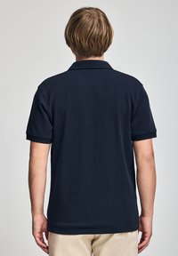 Camisa polo de color marino con mangas cortas, un collar plano y un ribete acanalado. Tela suave con un corte clásico, que presenta un dobladillo recto y aberturas laterales.