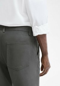 Dark gray pants with a smooth texture and a classic cut, featuring a back pocket and a visible waistband, paired with a white rolled sleeve shirt.