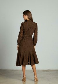 Rochie midi cu model maroniu, cu mâneci lungi, curea în talie și fustă evazată. Țesătură texturată și guler rotunjit în spate.