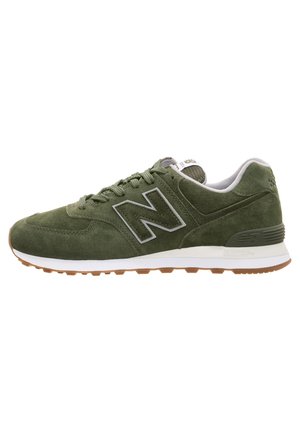 Zielony zamszowy sneaker z białą śródpodeszwą i gumową podeszwą zewnętrzną, z logo "N" po boku i sznurowadłami na górze.