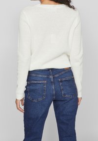 Pull blanc en maille avec motif texturé et poignets côtelés, associé à un jean en denim bleu avec poches et légère décoloration.