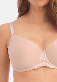 Beige beha met soepele, gepadde cups en kantdetails aan de onderkant. Verstelbare schouderbanden met een kleine strikaccent. Naadloos ontwerp.