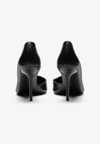 Zapatos de tacón alto de cuero negro con punta afilada, que presentan un diseño elegante y un tacón de aguja. Textura suave con acentos mínimos.