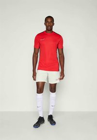 Crvena Nike atletska majica s crnim akcentima, uparena s bijelim kratkim hlačama. Igrač nosi crne kopačke i bijele čarape s plavim logom.