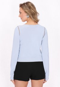Suéter azul claro de manga larga, con escote ribeteado y detalle de costura abierta en los hombros, combinado con pantalones cortos negros.