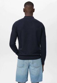 Suéter de punto navy con mangas largas, dobladillo acanalado y cuello. Combinado con unos pantalones cortos de mezclilla azul claro, que cuentan con bolsillos traseros y un corte relajado.
