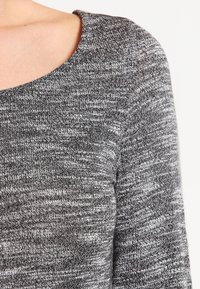 Szary melanżowy top z długim rękawem i okrągłym dekoltem; tkanina wygląda na miękką i teksturowaną, z subtelnymi odcieniami koloru i wzoru.