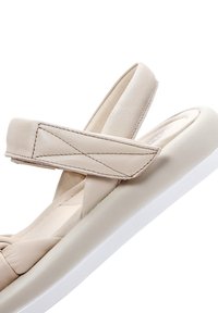 Beige leren sandaal met een dikke witte zool, voorzien van kruislingse banden en gestikte accenten, met een gladde textuur en eenvoudig ontwerp.