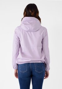 Giacca impermeabile di un leggero lavanda con cappuccio, polsini elasticizzati e una vestibilità rilassata, abbinata a jeans in denim blu scuro.