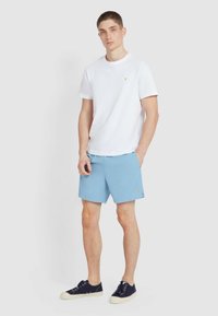 Biała koszulka, niebieskie szorty i granatowe sneakersy. Koszulka ma małe logo; szorty mają gładką teksturę i subtelne szwy.