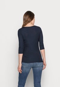 Dunkelblaues enges Oberteil mit Dreiviertelärmlen, gerippter Textur und rundem Ausschnitt, kombiniert mit hellblauen Jeans mit Gesäßtaschen.