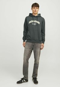 Ciemnoszara bluza z kapturem z przednią kieszenią, z białym napisem i logo "JACK & JONES". Połączona z wyblakłymi szarymi dżinsami i czarnymi sneakersami.