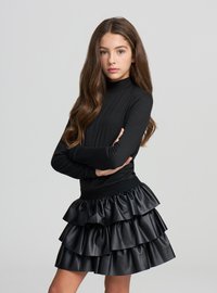 Top nero a maniche lunghe abbinato a una gonna nera in ecopelle con balze sovrapposte, che creano un design strutturato e voluminoso.