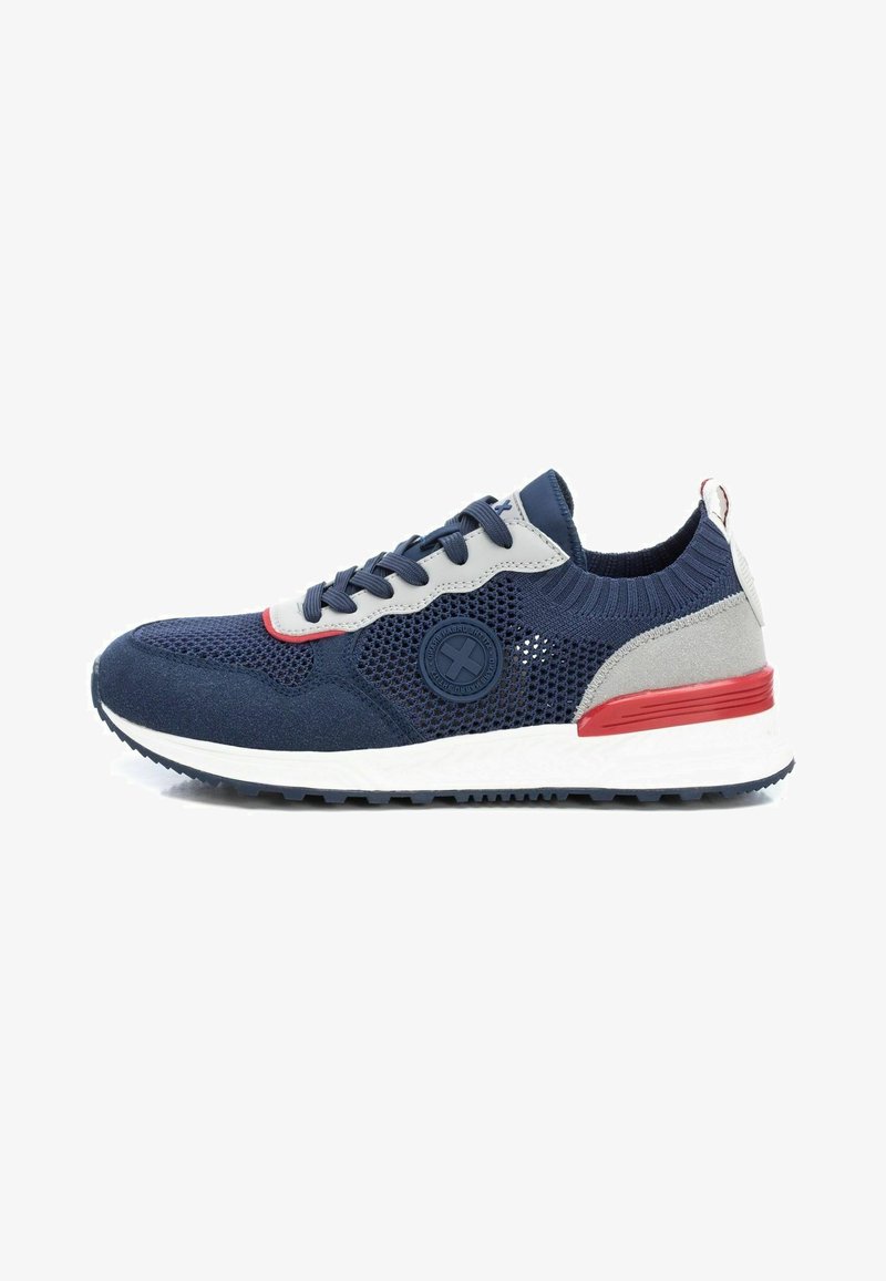Zapatilla de deporte azul marino con materiales de malla y ante; presenta acentos grises, suela blanca y detalles rojos; puntera redondeada y parte superior texturizada.