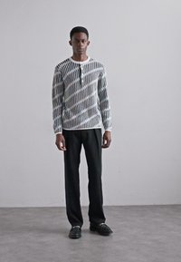 Μαύρη και λευκή μπλούζα με μακριά μανίκια και κάθετες καθώς και διαγώνιες ρίγες; συνδυασμένη με μαύρο παντελόνι και μαύρα παπούτσια; υφασμάτινη υφή.