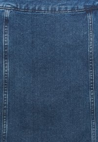 Närbild av blå denimtyg med vertikala sömmar och texturerad vävstruktur.