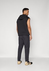 Sort ærmeløs hættebluse med hætte, parret med mørkegrå bukser og beige sko. Enkelt design med en afslappet pasform og strækbart materiale.