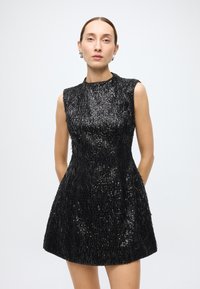 Black sleeveless dress with textured fabric featuring vertical sequins and beaded accents, flared skirt, and high neckline.