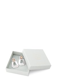 Pendientes en tono plateado con un diseño geométrico en capas, con una gema rectangular marrón en la parte superior, presentados en una caja de joyería gris.