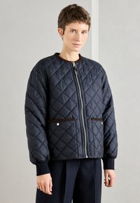 Jūras zilas krāsas quilted jaka ar rāvējslēdzēju, brūniem akcentiem un divām priekšējām kabatām. Iezīmējas ar ribotām piedurknēm un apaļu kaklu.