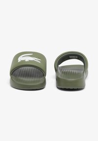 Green rubber slide sandals with a textured insole and wide strap featuring a white crocodile logo. Open back design for easy wear.