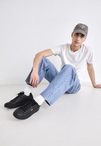 Baskets noires en cuir texturé, avec des semelles blanches et un logo discret. Associées à un jean en denim bleu clair et un t-shirt blanc.