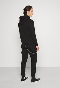 Svart hettegenser, svarte cargo-bukser med aksentstropper, slim-fit design og svarte høyhælte sneakers. Kvalitet i bomull, glatt tekstur.