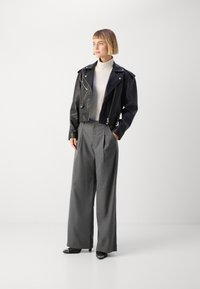Black leather cropped jacket, gray pleated wide-leg trousers, cream turtleneck, and black pointed-toe shoes, presented in a neutral background.