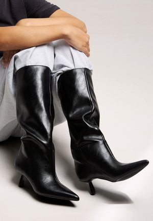 Stivali neri al ginocchio realizzati in pelle liscia, con punta affilata e tacco slim e affusolato. Il design presenta morbidi dettagli arricciati.