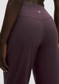 Augsta vidukļa plūmju purpura legingi, izgatavoti no gludas, elastīgas auduma, ar minimālu šuvju detaļu skaitu un nelielu logotipu aizmugurē pie vidukļa.