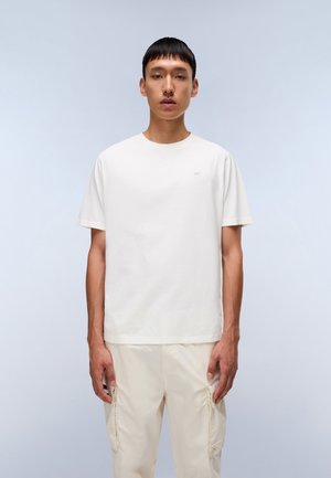White cotton t-shirt with a classic crew neck and short sleeves, featuring a subtle logo on the left chest area. Styled with light pants.