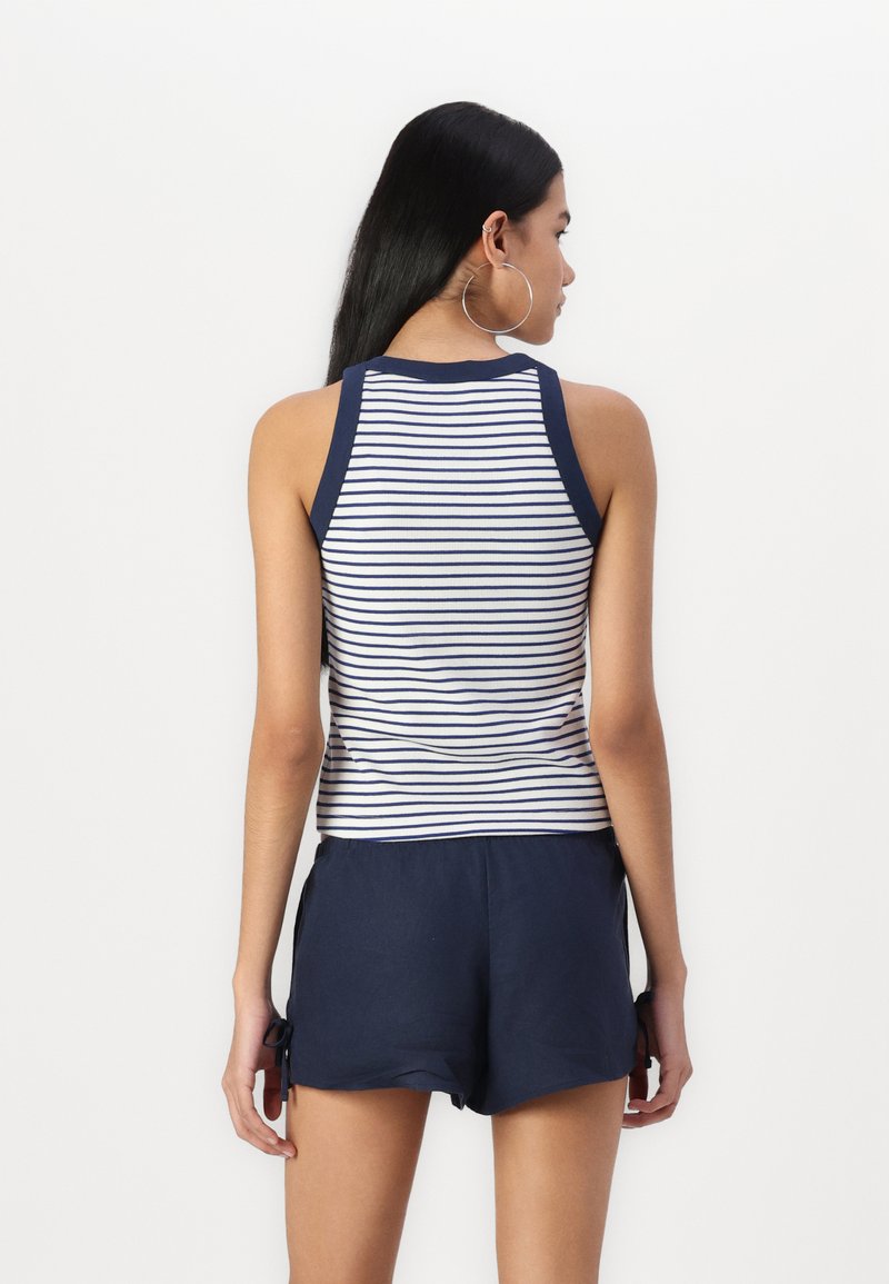 Top sin mangas a rayas con detalles en azul marino, combinado con pantalones cortos azul marino con lazos laterales. El tejido parece ligero y casual.