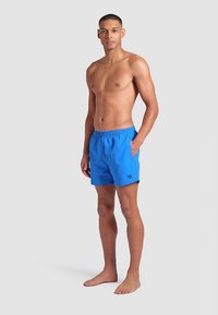 Blå badshorts i lätt tyg med resår i midjan och sidofickor. Slät yta, normal passform, logodetalj på låret.