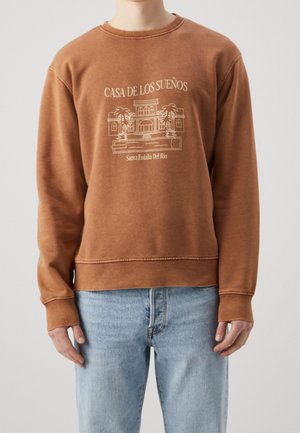 Sudadera marrón con cuello redondo, que presenta un gráfico de una casa y el texto "CASA DE LOS SUEÑOS". Puños y dobladillo acanalados.