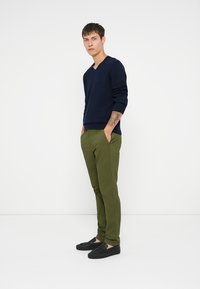 Pull en V bleu marine, pantalon vert tapered et chaussures noires à enfiler. Design minimaliste sans motifs visibles. Texture de tissu lisse.