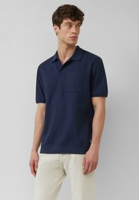 Navyblauwe polo met een textuur van verticale streepjes, korte mouwen en een borstzak. Geribbelde kraag en zoomdetails.