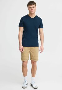 Marine blå V-hals T-skjorte, kortermet, kombinert med khaki rullede shorts. Brukt med hvite sokker og svart-hvite sportsko.