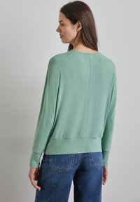 Un pull vert menthe avec une coupe décontractée, des poignets et un bas côtelés, et une couture arrière droite. Accordé avec un jean en denim bleu.