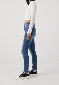 Úzké modré džíny s mírným vzestupem pasu, spárované s bílým dlouhým crop topem a černými teniskami s červenými akcenty třešní.