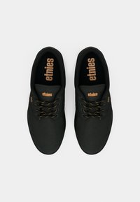 Μαύρα καμβά παπούτσια με σχέδιο σε στρογγυλή μύτη, αντίθετες καφέ κορδόνες και λογότυπο "etnies" στη γλώσσα και στο πλάι. Υφασμάτινη επιφάνεια για πρόσφυση.