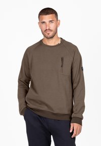 Sudadera verde oliva con mangas raglán, cuello redondo, bolsillo con cremallera en el pecho y puños acanalados. Tejido suave con un corte holgado.
